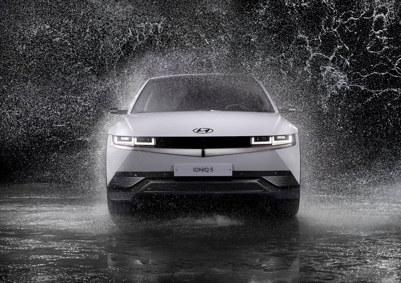 Dynamic front view of a Hyundai Ioniq 5 splashing through rain, captured in black and white.